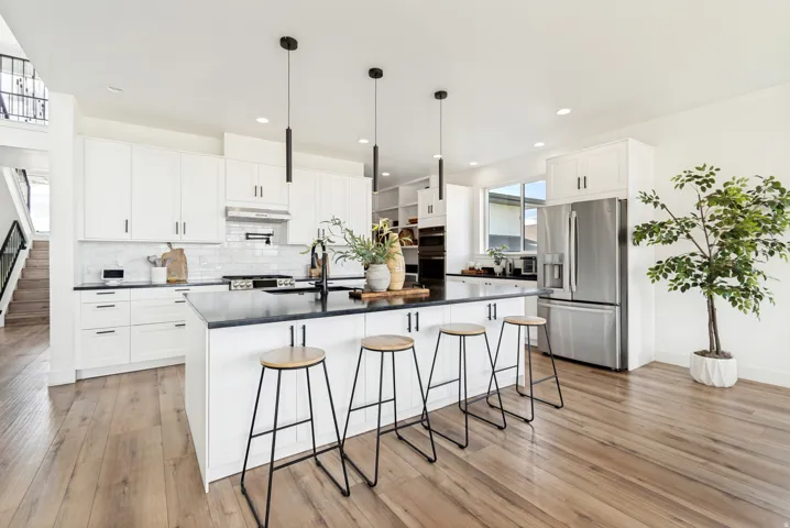 Modern kitchen featuring a large central island with seating, white shaker cabinetry, stainless steel appliances, and wood-finish flooring