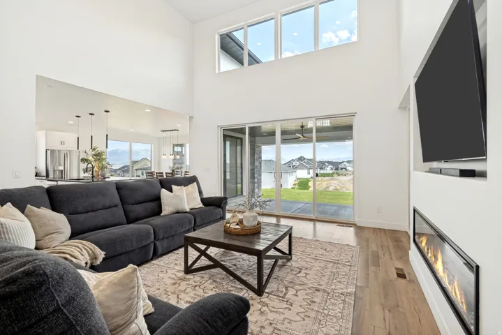 Expansive living space featuring a soaring ceiling, wood-finish flooring, a linear fireplace, and large sliding glass doors opening to the exterior