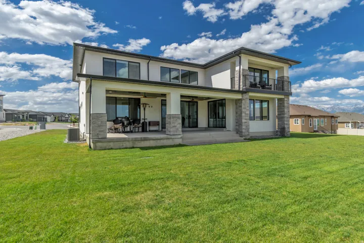 Spacious rear exterior featuring a covered patio, second-story balcony with metal railing, and an expansive green lawn