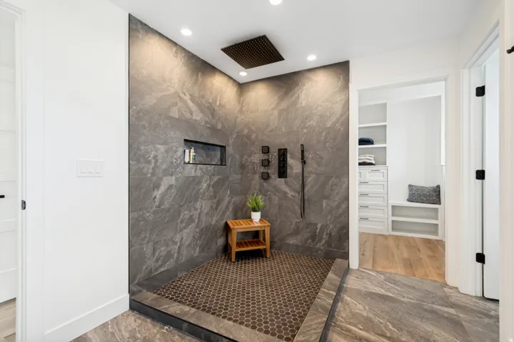 Spacious walk-in shower featuring large format gray stone-finish wall tile, a rain showerhead, and matte black fixtures