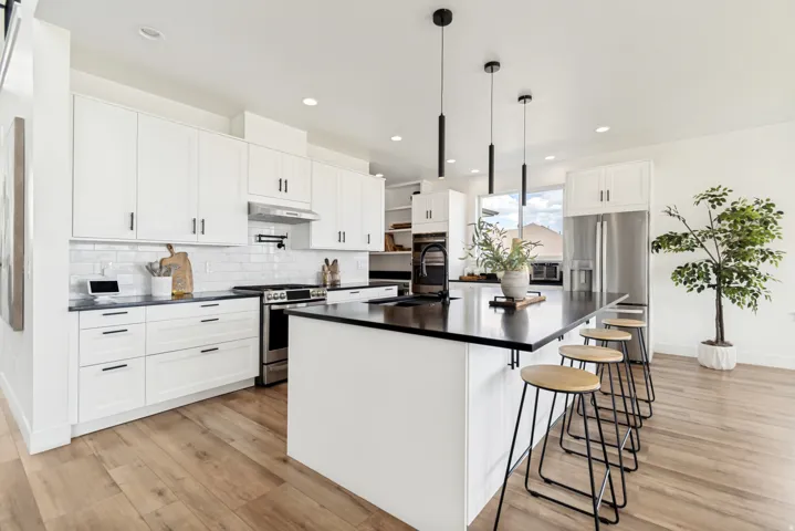 Modern kitchen featuring a large island with dark countertops, white cabinetry, stainless steel appliances, wood-finish flooring, and white subway tile backsplash