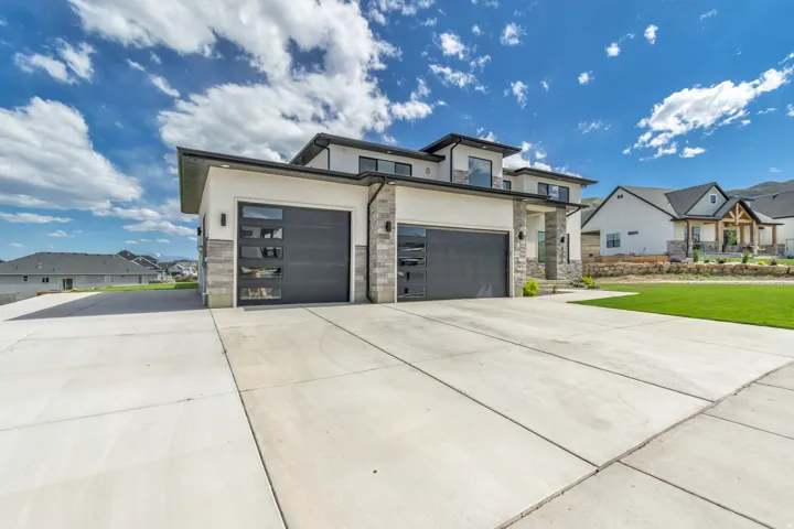 Modern architectural design featuring a multi-level facade, stone veneer accents, flat rooflines, a two-car garage with contemporary glass-panel doors, and an expansive concrete driveway
