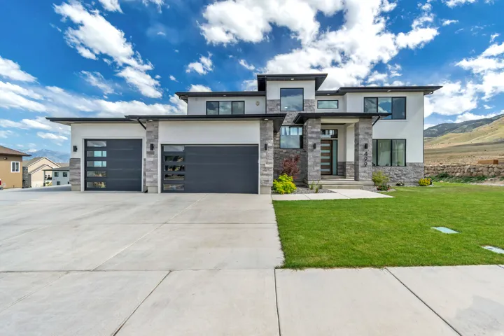 Modern exterior featuring a prominent entry, stone accents, multiple garage doors with window panels, a concrete driveway, and a landscaped lawn