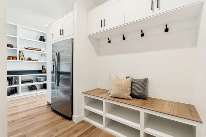 Built-in mudroom bench with wood-finish top and integrated storage cubbies, complemented by overhead white shaker cabinetry with matte black hardware and wall-mounted hooks