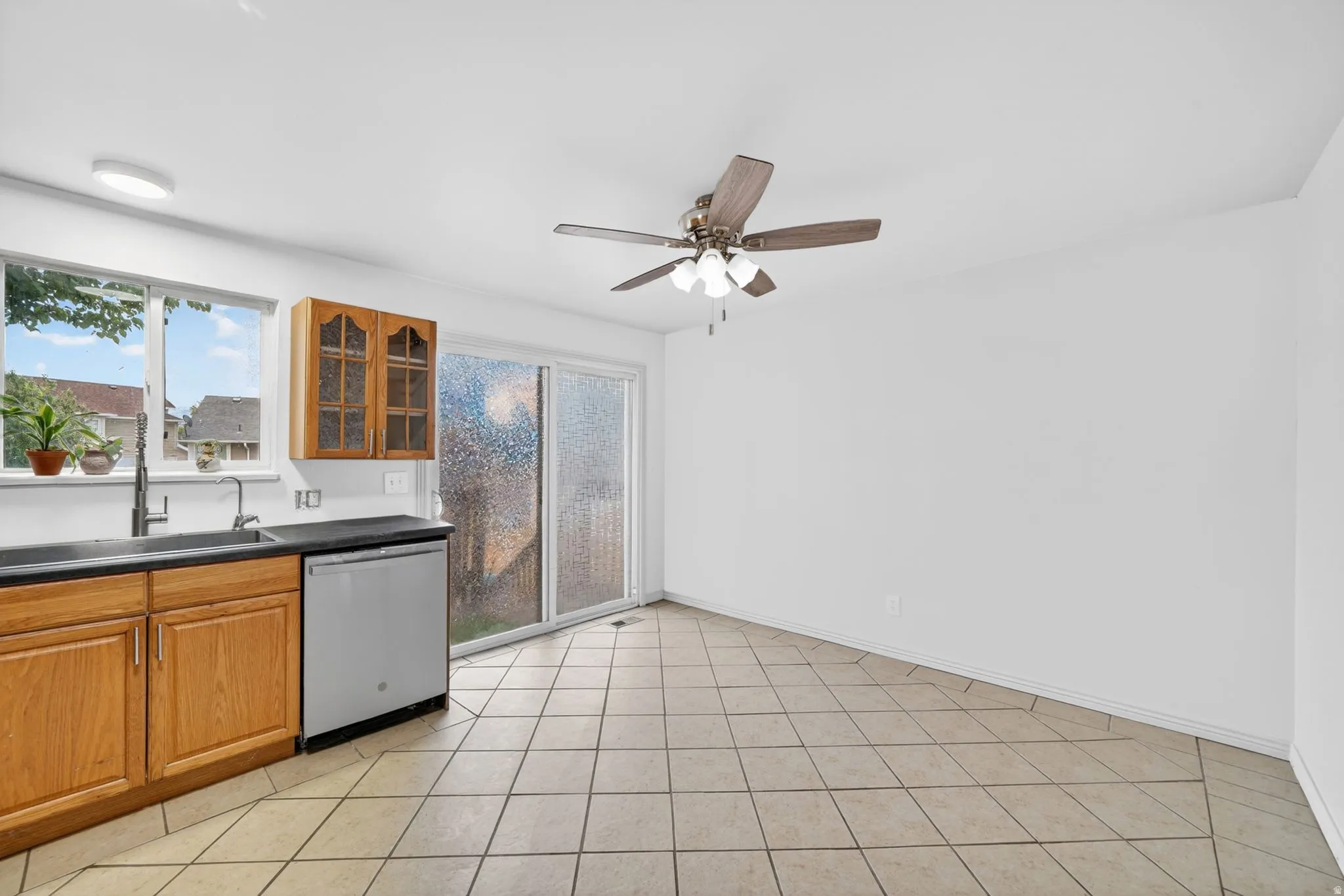 Kitchen area featuring light wood cabinetry, dark countertops, a stainless steel dishwasher, a window over the sink, and a sliding glass door