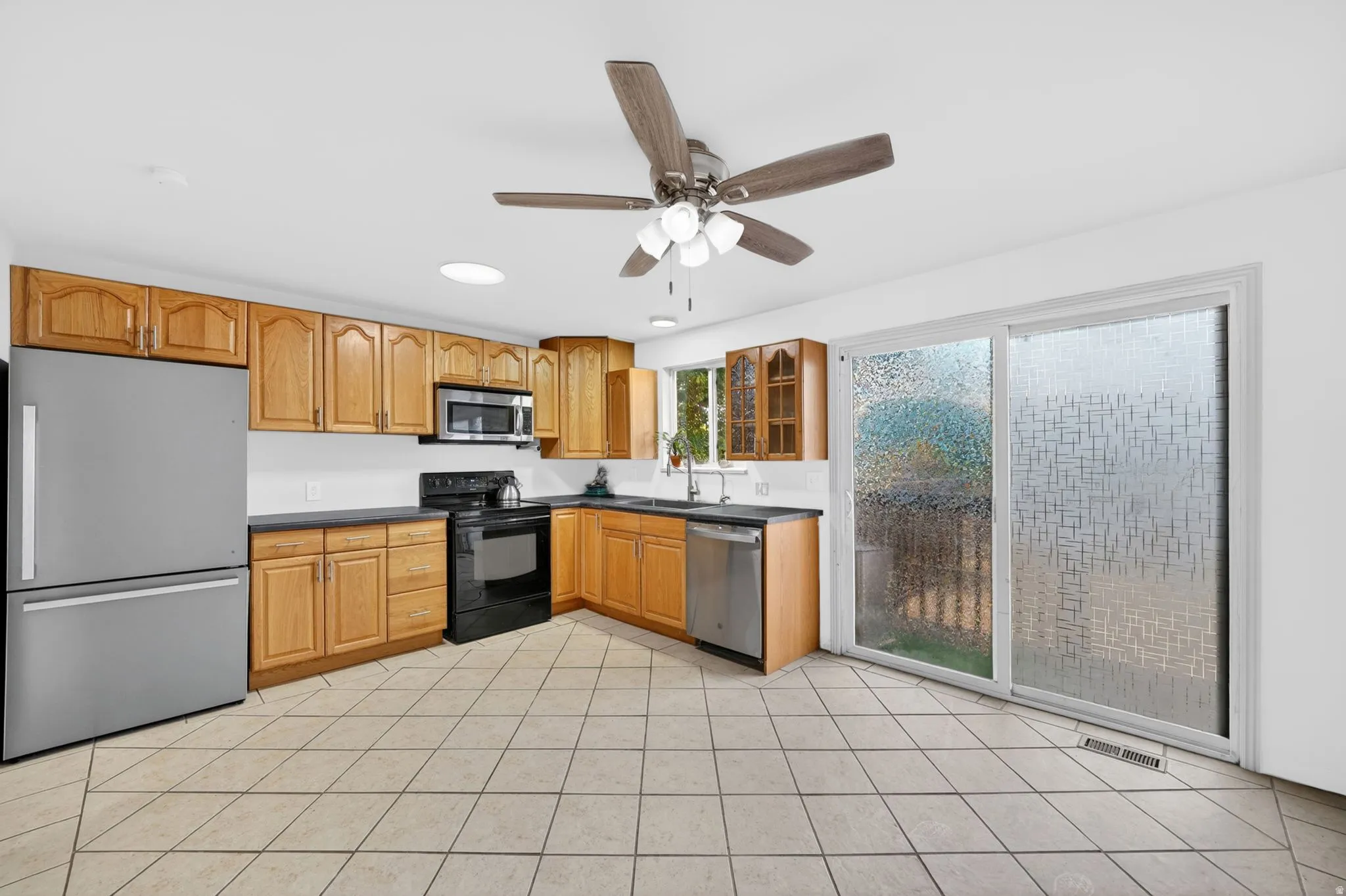 Kitchen featuring light wood cabinetry, dark countertops, and stainless steel appliances including a refrigerator, microwave, and dishwasher