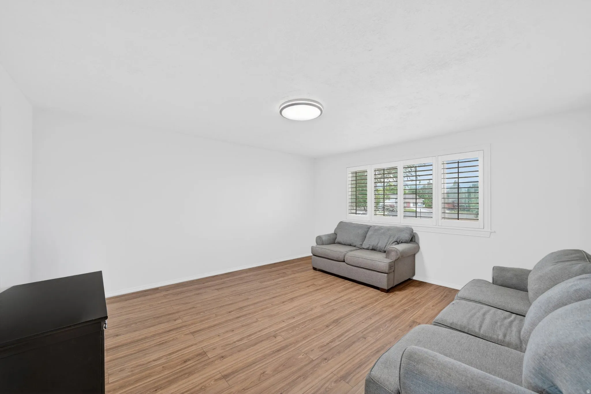 Spacious room featuring wood-finish flooring, white walls, and a multi-pane window with louvered shutters