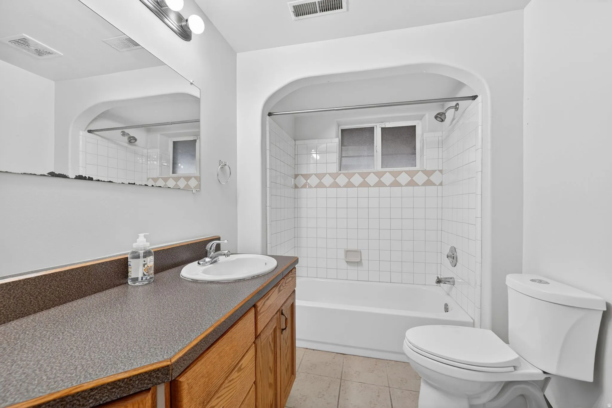 Bathroom featuring a wood-finish vanity with a laminate countertop, an integrated sink, and an arched shower-tub combination with white subway tile surround and decorative accents