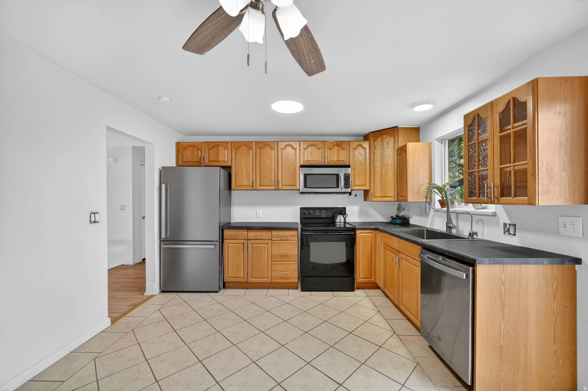 Kitchen featuring wood cabinetry, stainless steel appliances, black countertops, and a tile floor