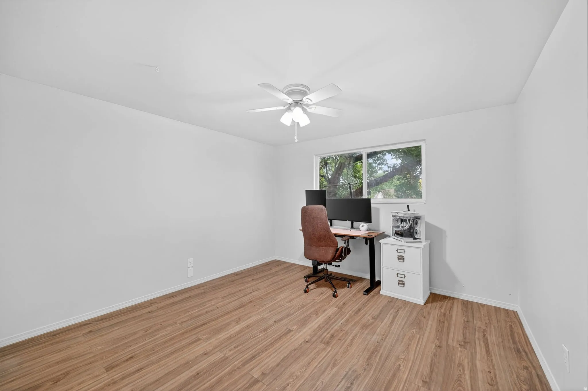 Spacious room with wood-finish flooring, white walls, and a ceiling fan