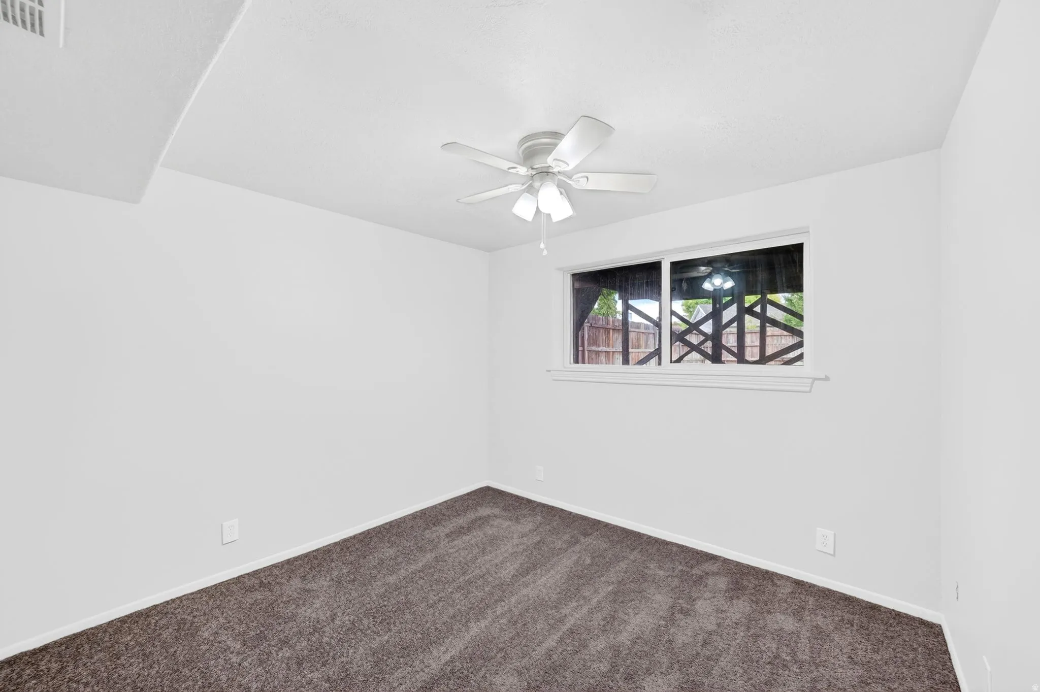 Carpeted room featuring a ceiling fan with integrated lighting, a window with white trim, and white walls