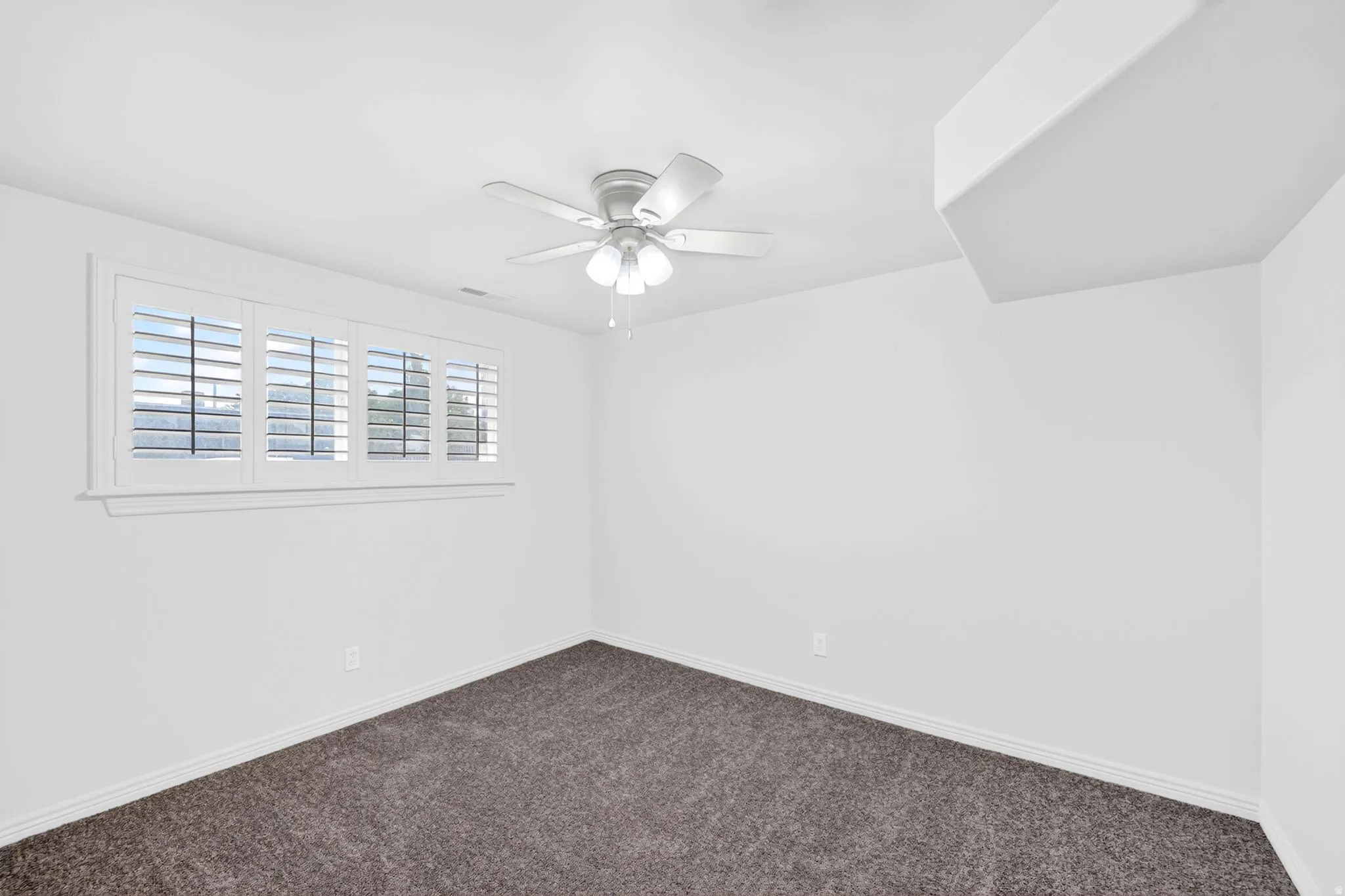 Carpeted interior space featuring a window with white louvered shutters, a ceiling fan with integrated lighting, and white baseboards