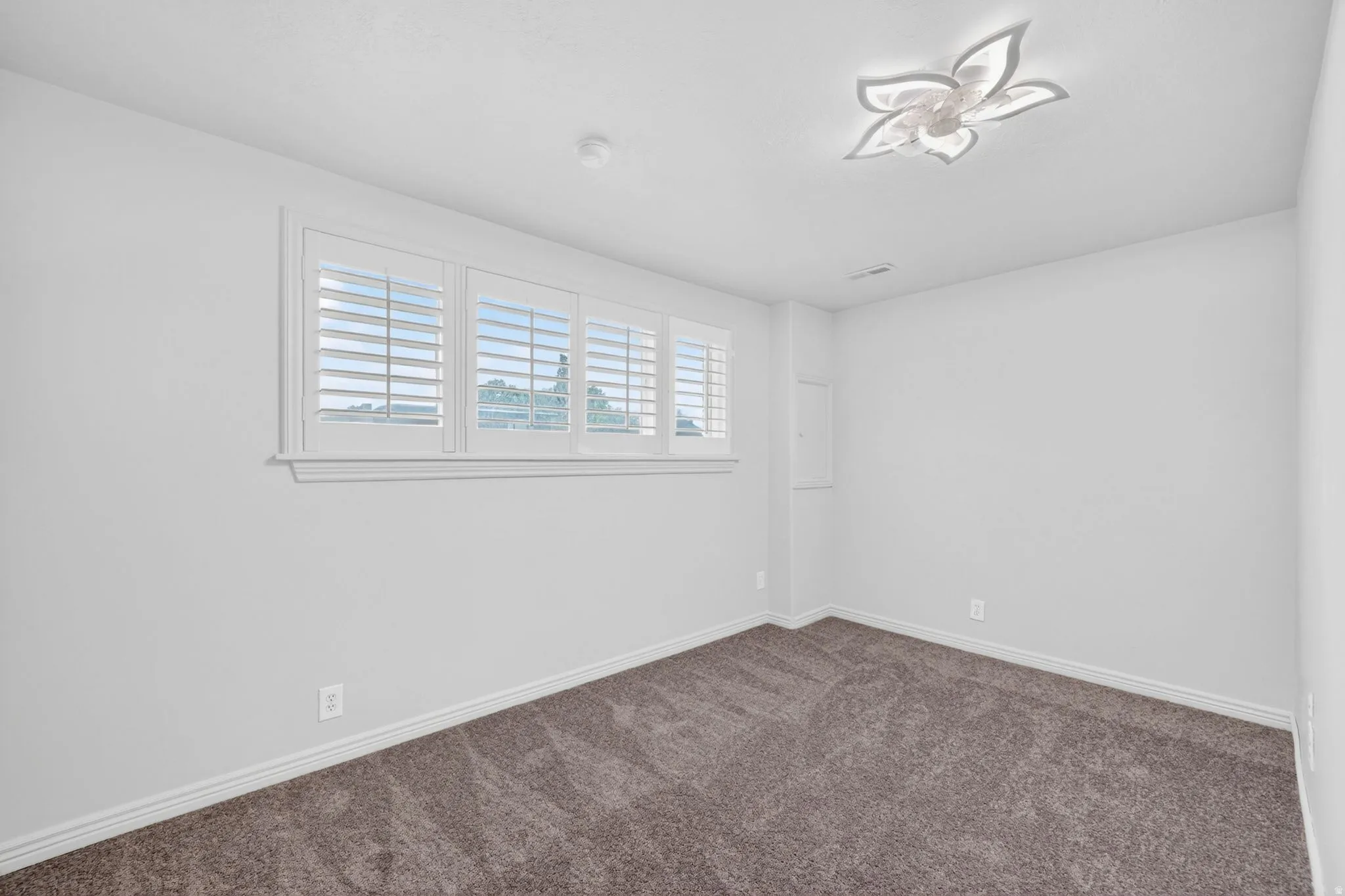 Neutral-toned room with plush carpet flooring, white walls, and a decorative ceiling light fixture