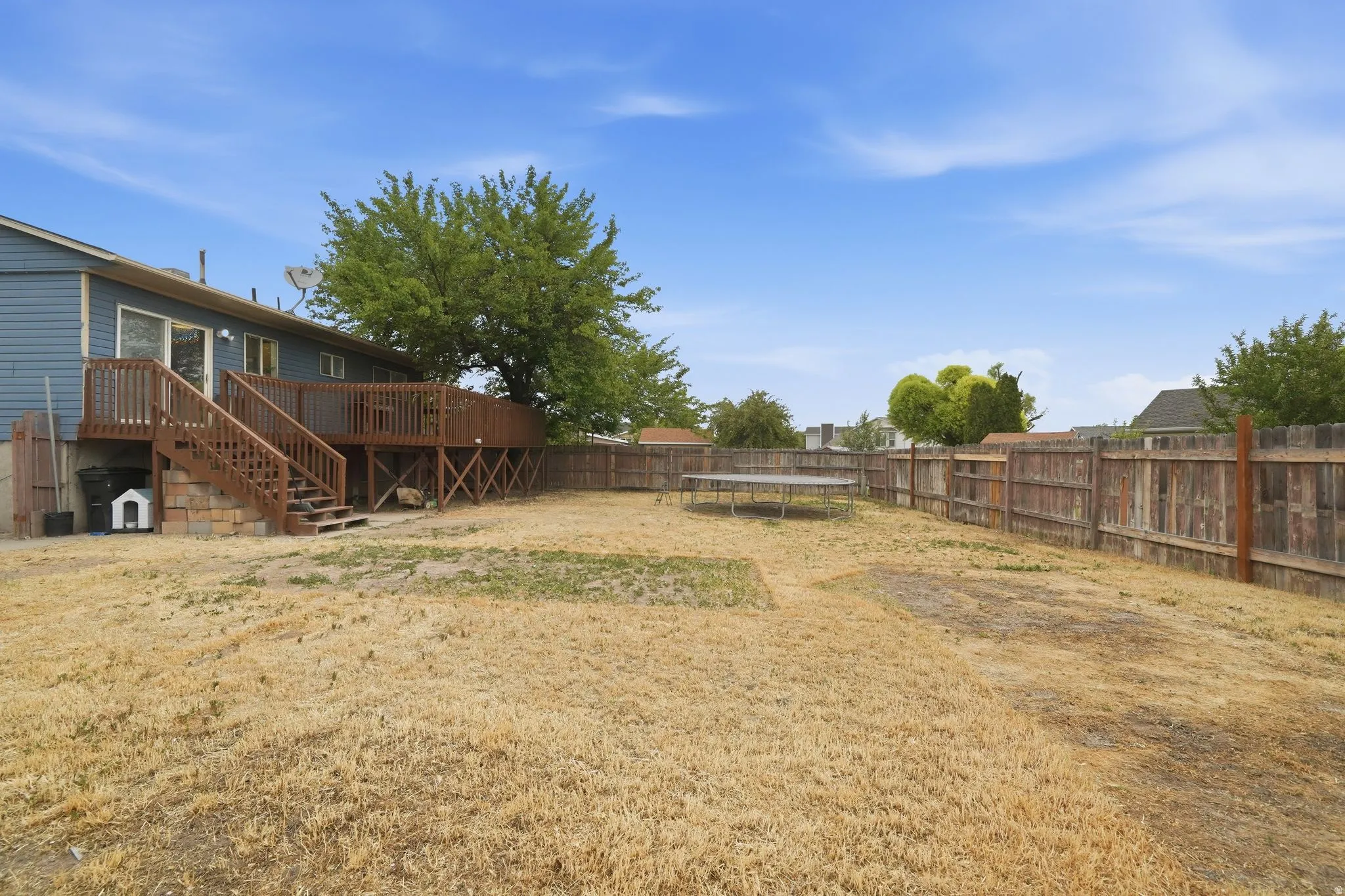 Expansive backyard featuring a wood privacy fence and a large wood deck with stairs