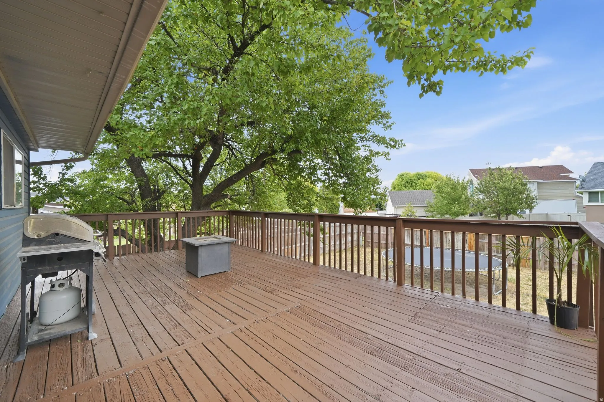 Expansive outdoor deck featuring wood flooring and railings, a covered portion for shade, and mature surrounding trees
