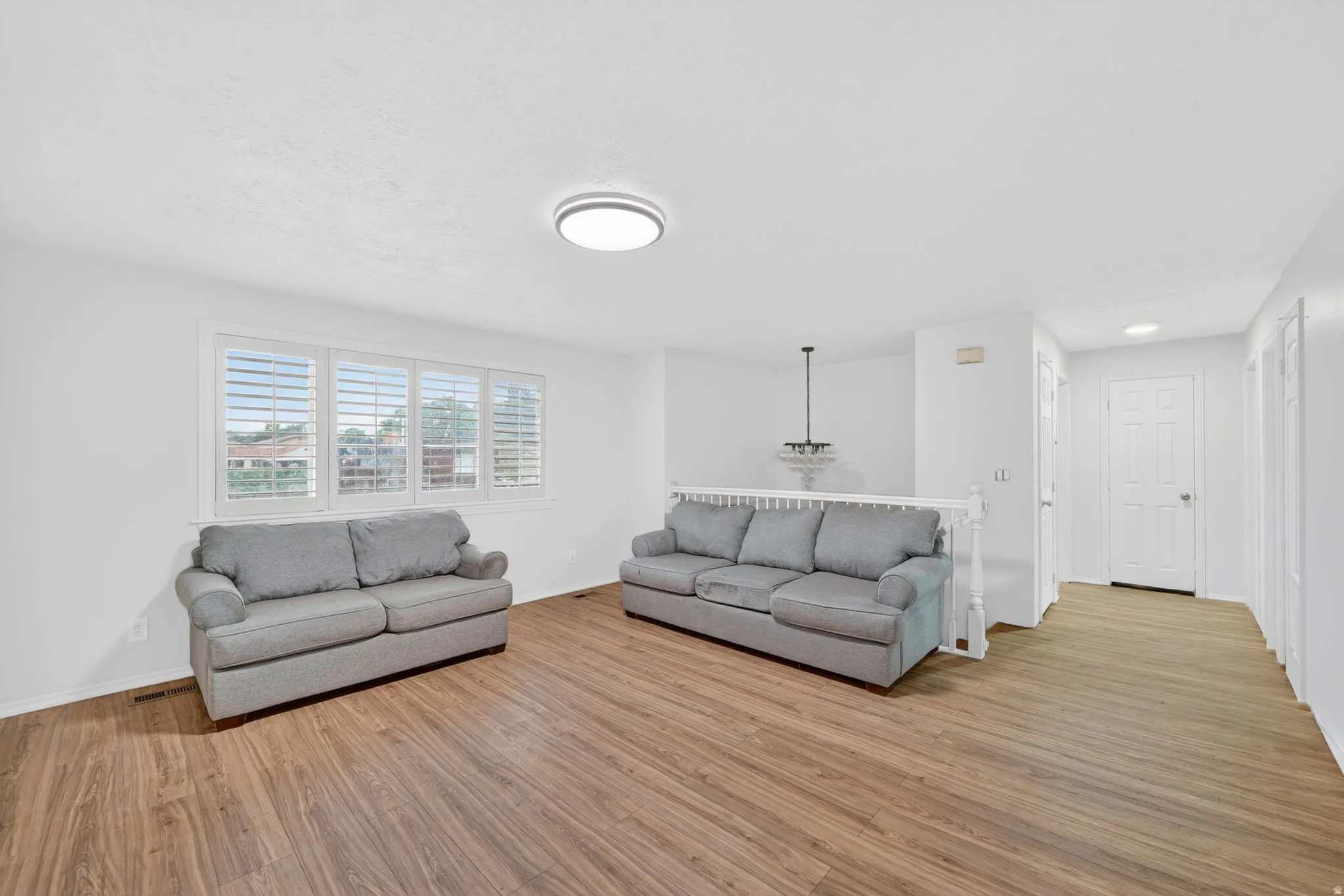 Bright living area featuring wood-finish flooring, white walls, and a large window with plantation shutters