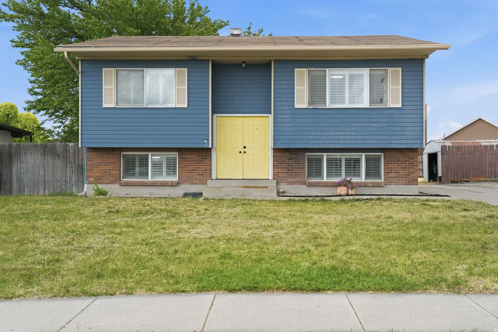 Split-level exterior featuring blue horizontal siding, brick accents, a distinctive yellow double-door entry, and multiple windows with louvered shutters