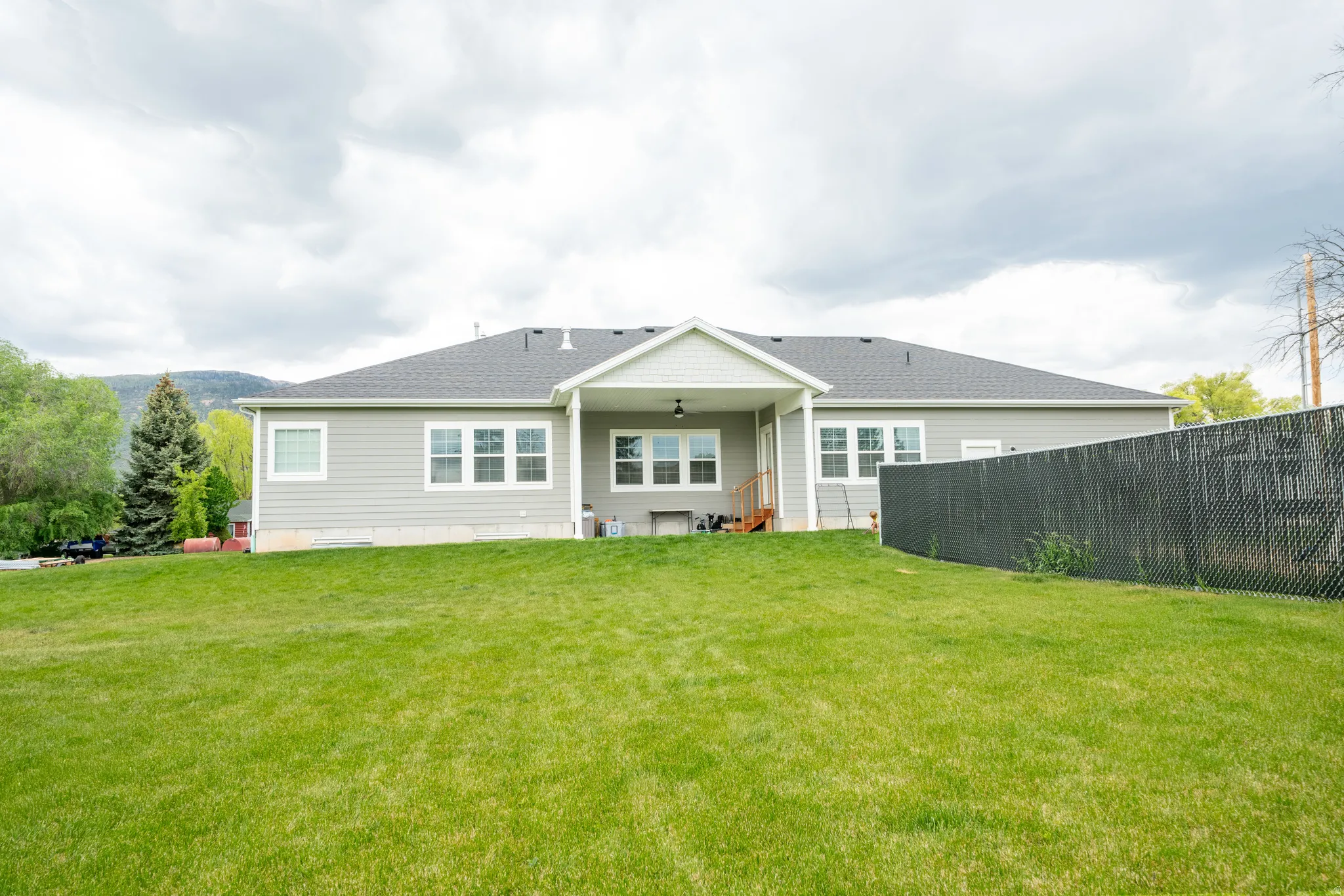 Expansive backyard featuring a manicured lawn, a covered patio, and a chain-link fence with privacy slats.