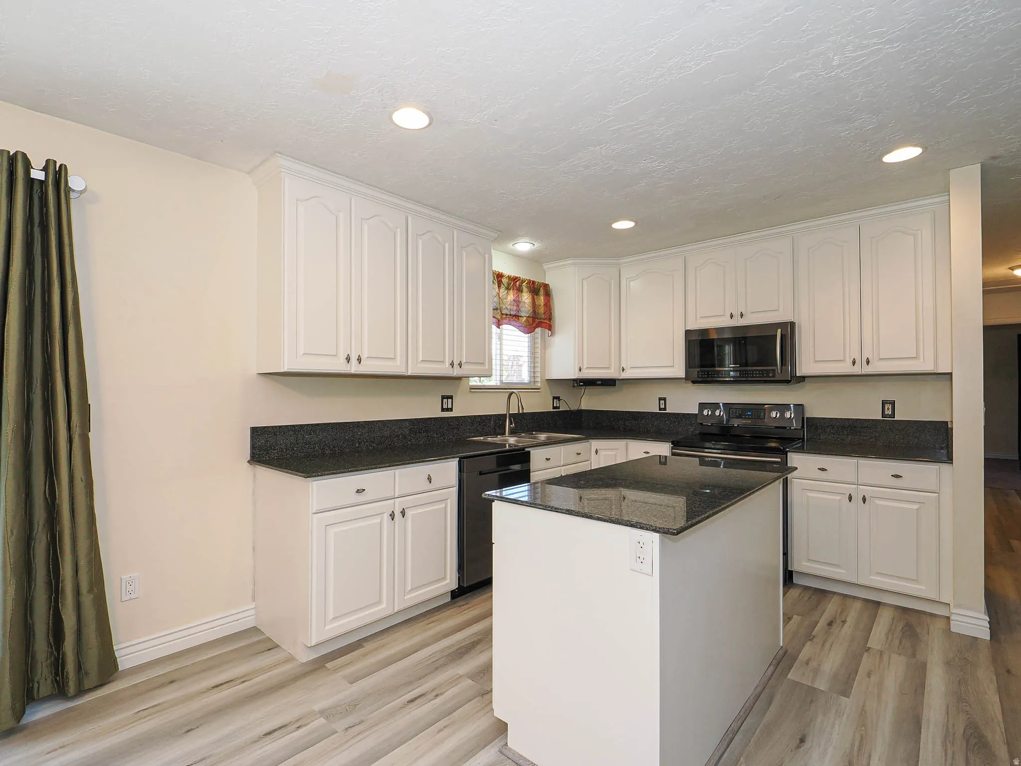 Kitchen featuring white cabinetry, dark stone countertops, stainless steel appliances, a central island, and wood-finish flooring