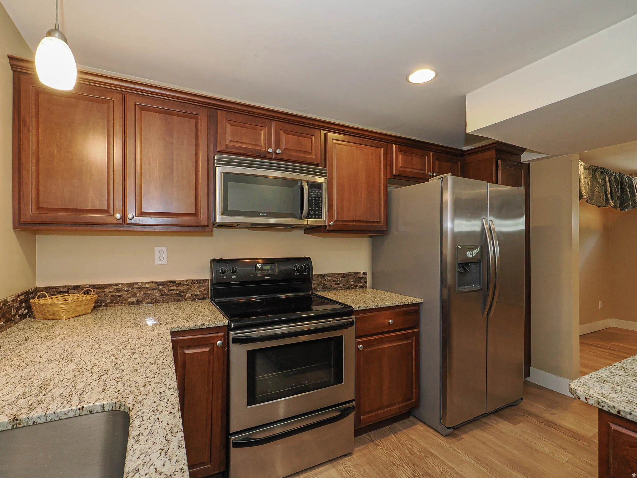 Kitchen featuring wood-finish cabinetry, light-toned granite countertops, and a tiled backsplash