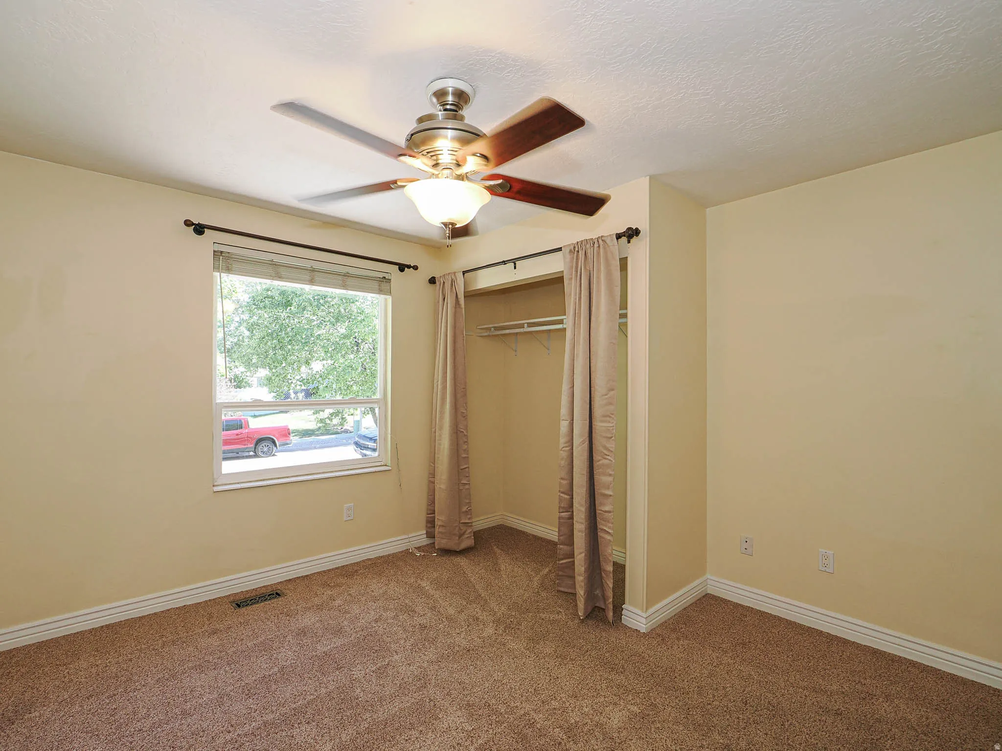 Carpeted room featuring a ceiling fan with integrated lighting, a window with a street view, and a recessed closet space
