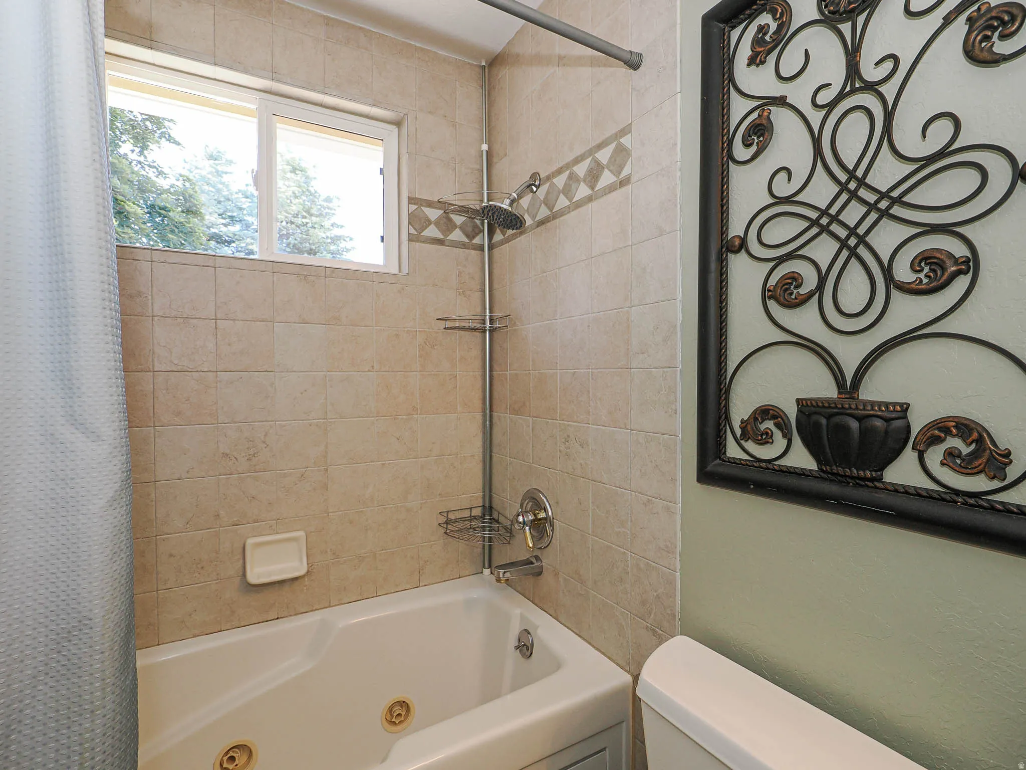 Bathtub with integrated jets, surrounded by beige square tiles featuring a decorative accent band