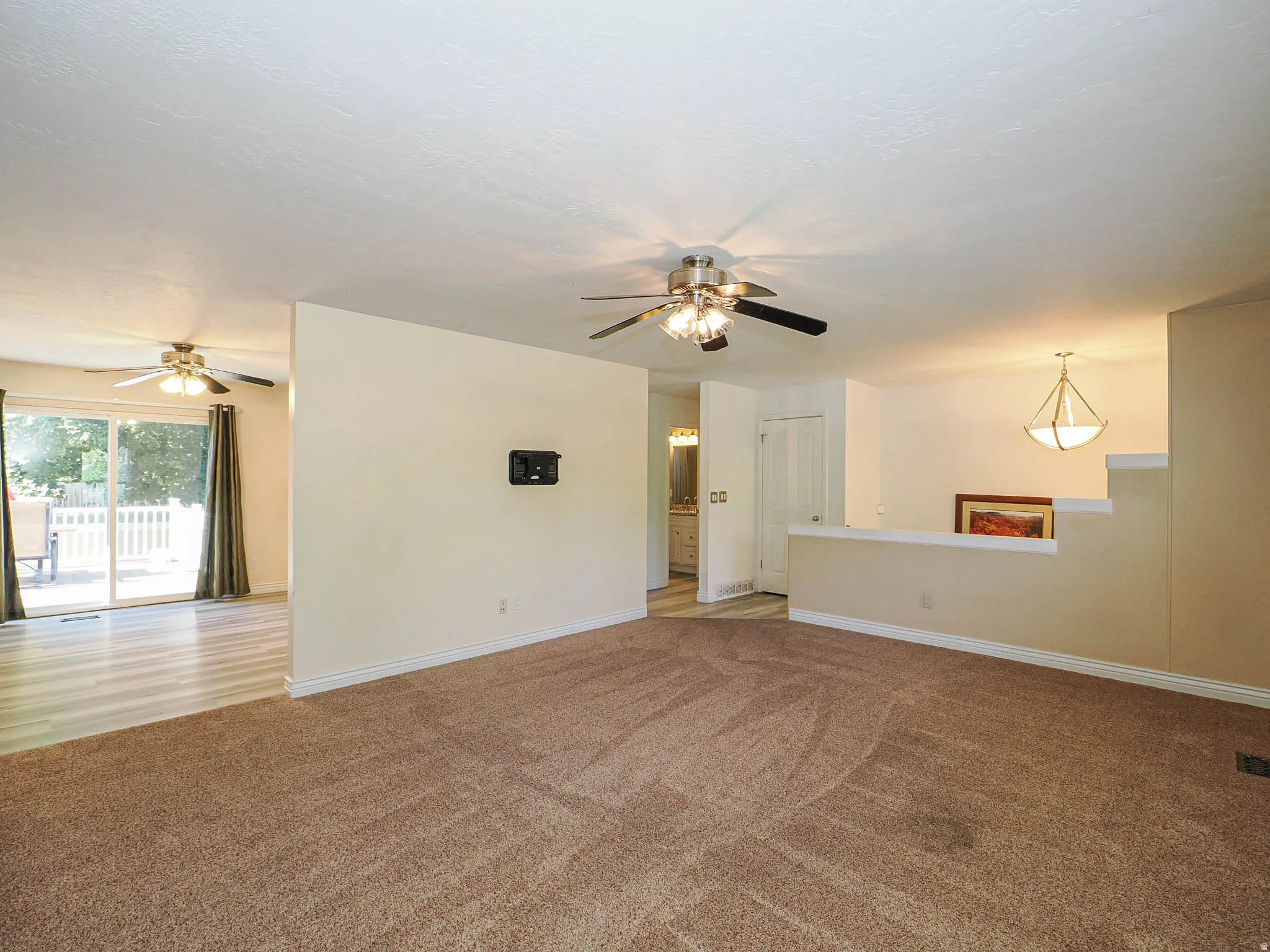 Spacious living area featuring neutral carpeting and a ceiling fan with integrated lighting