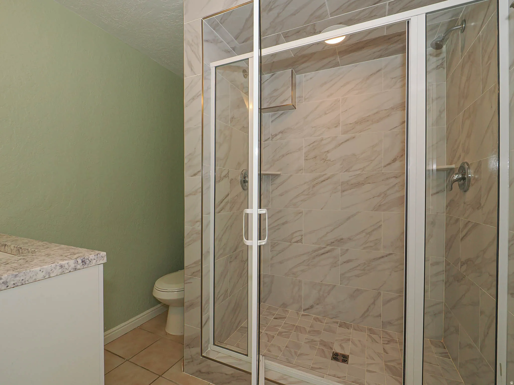 Glass-enclosed shower with tile surround and integrated shelving, featuring a complementary mosaic tile shower pan
