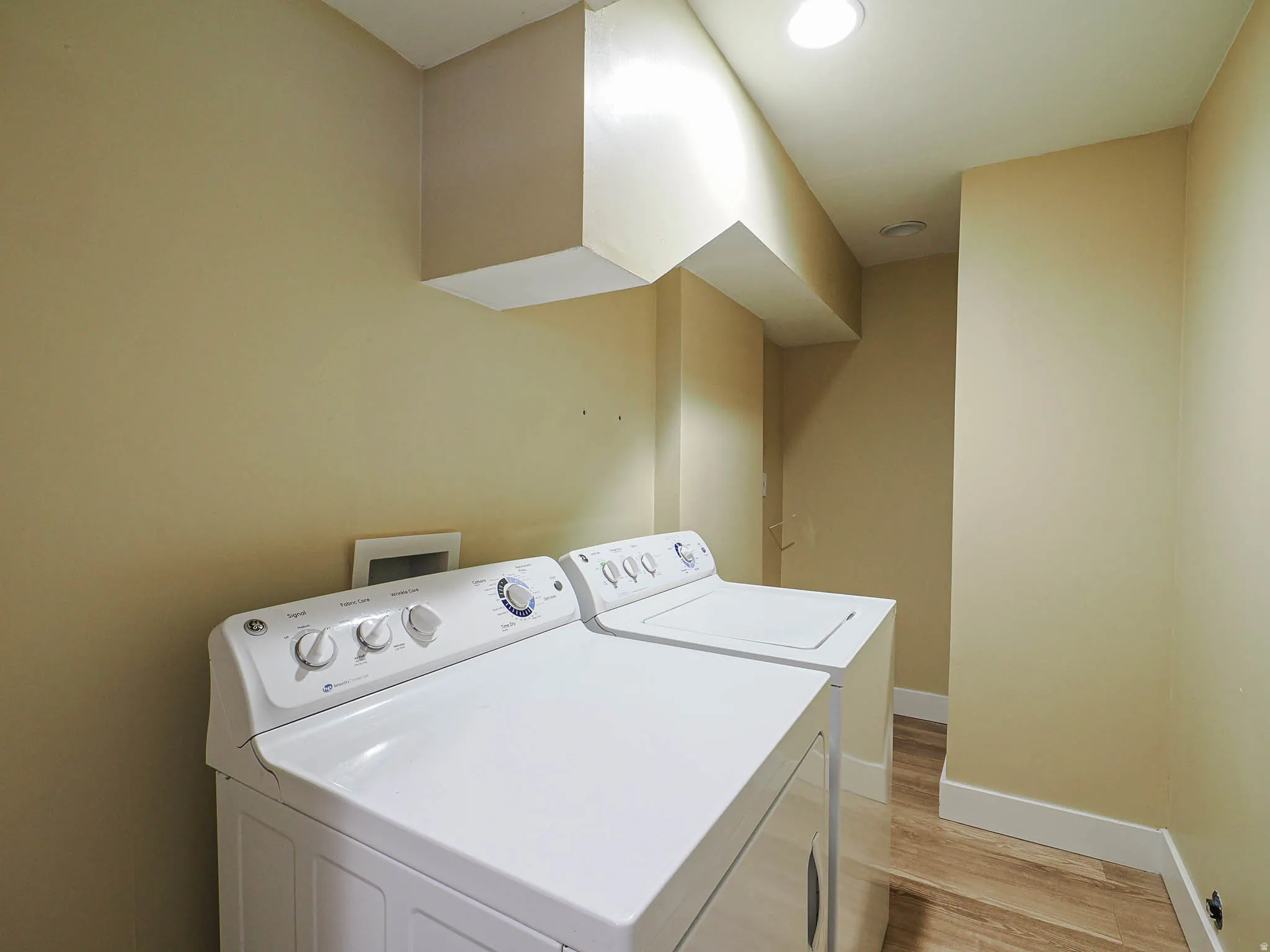 Dedicated laundry area featuring wood-finish flooring, light-toned walls, and recessed lighting