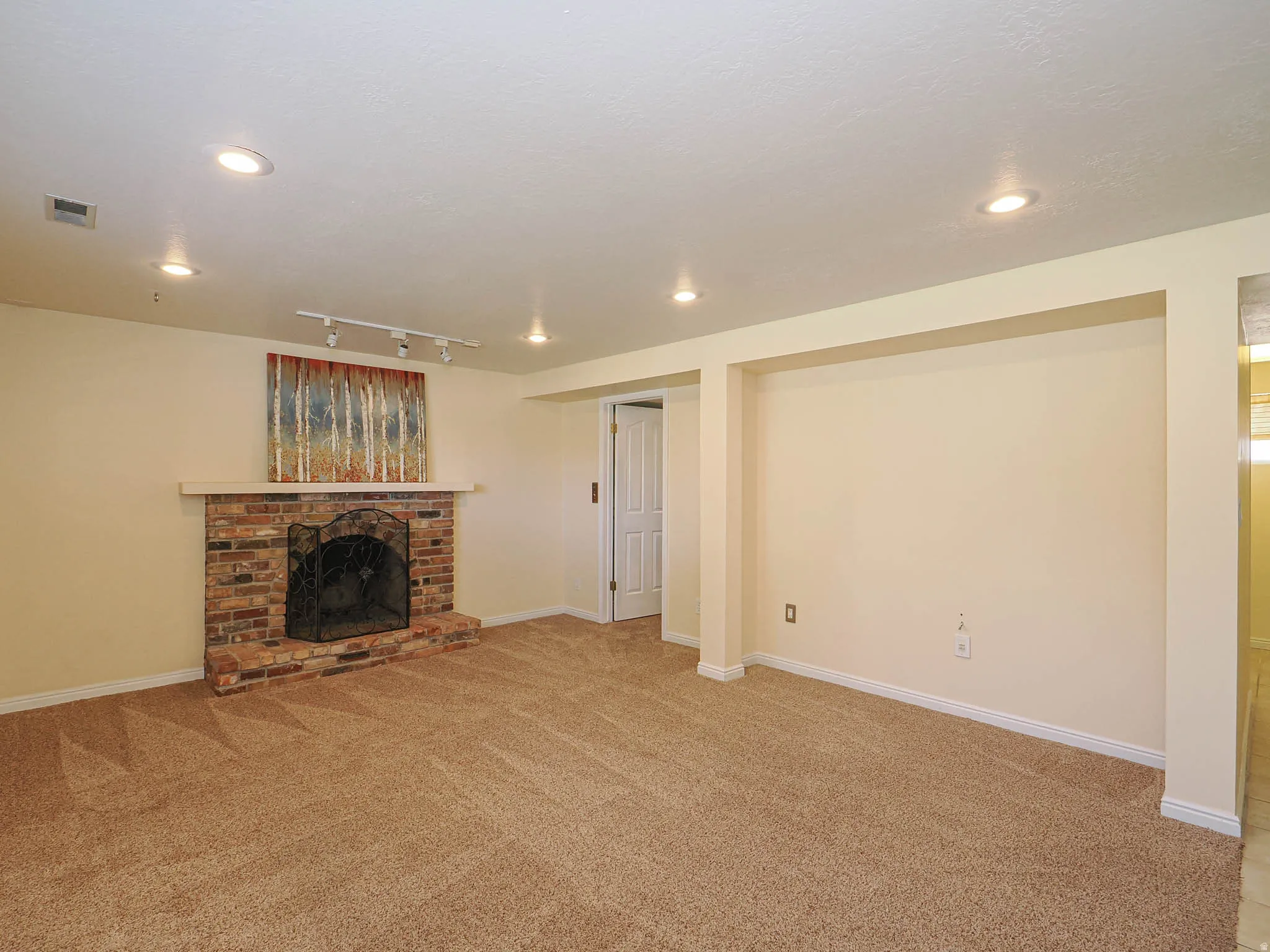 Spacious room featuring a brick fireplace with a white mantel, recessed lighting, and track lighting