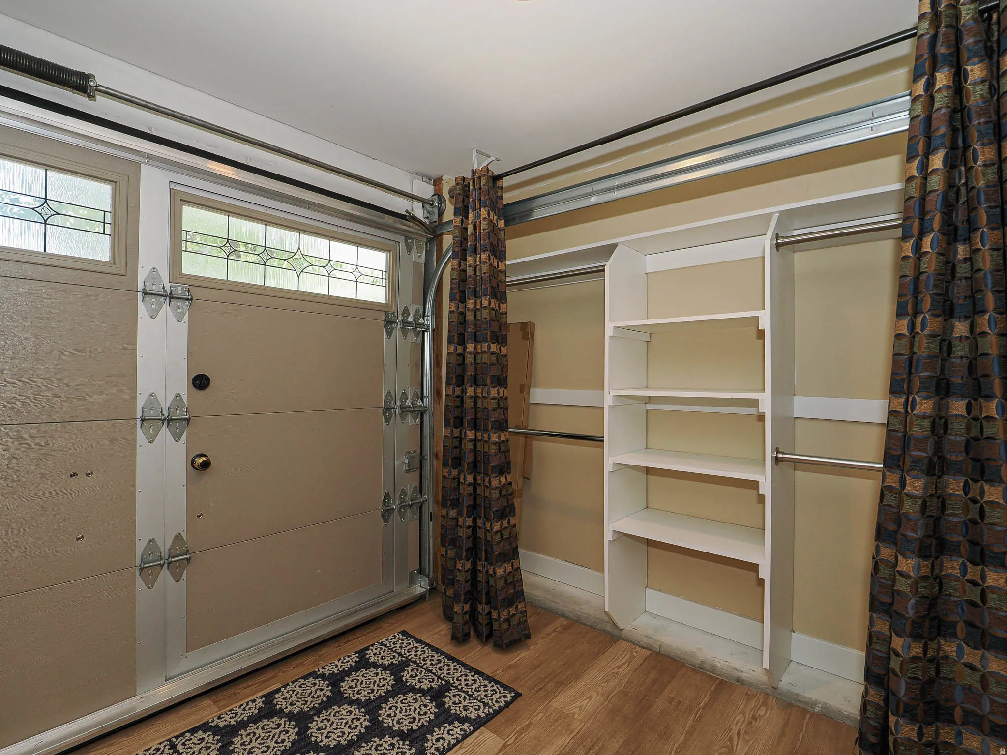 Garage space featuring a paneled door with decorative glass inserts, wood-finish flooring, and built-in white shelving units