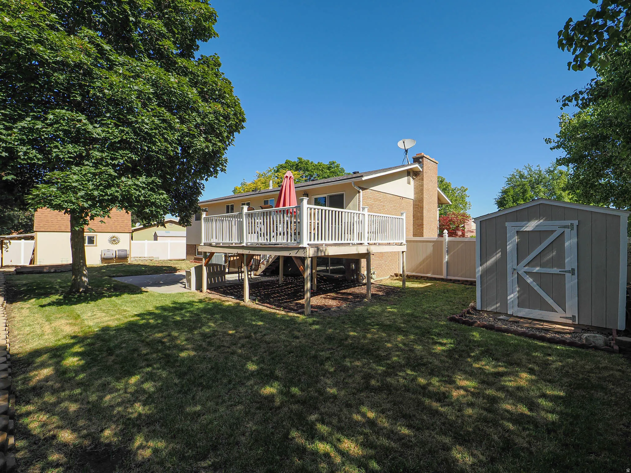Expansive backyard featuring a multi-level wood deck with white railings, a detached storage shed, privacy fencing, and mature trees