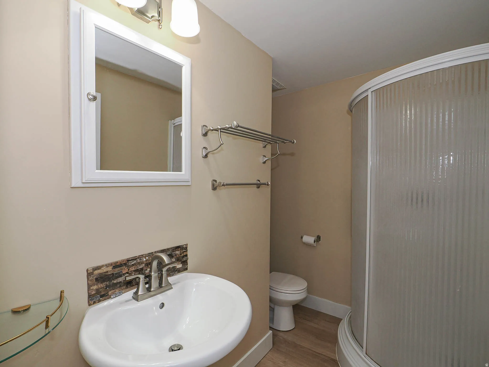 Bathroom featuring a white wall-mounted sink, mosaic tile backsplash, brushed nickel faucet, and a curved glass-enclosed shower