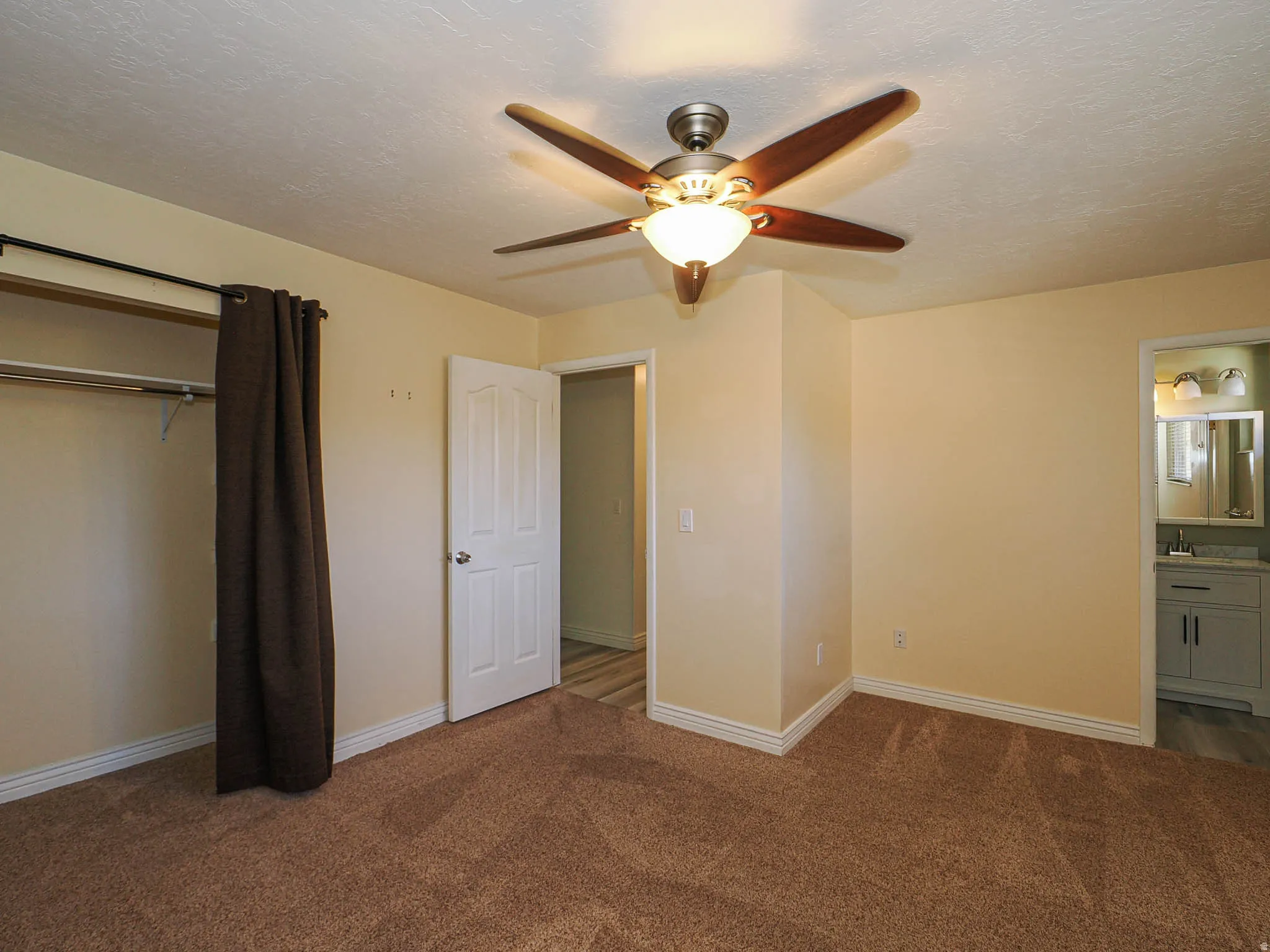 Carpeted bedroom with a ceiling fan light fixture, an open closet area with hanging rod, and a white paneled door