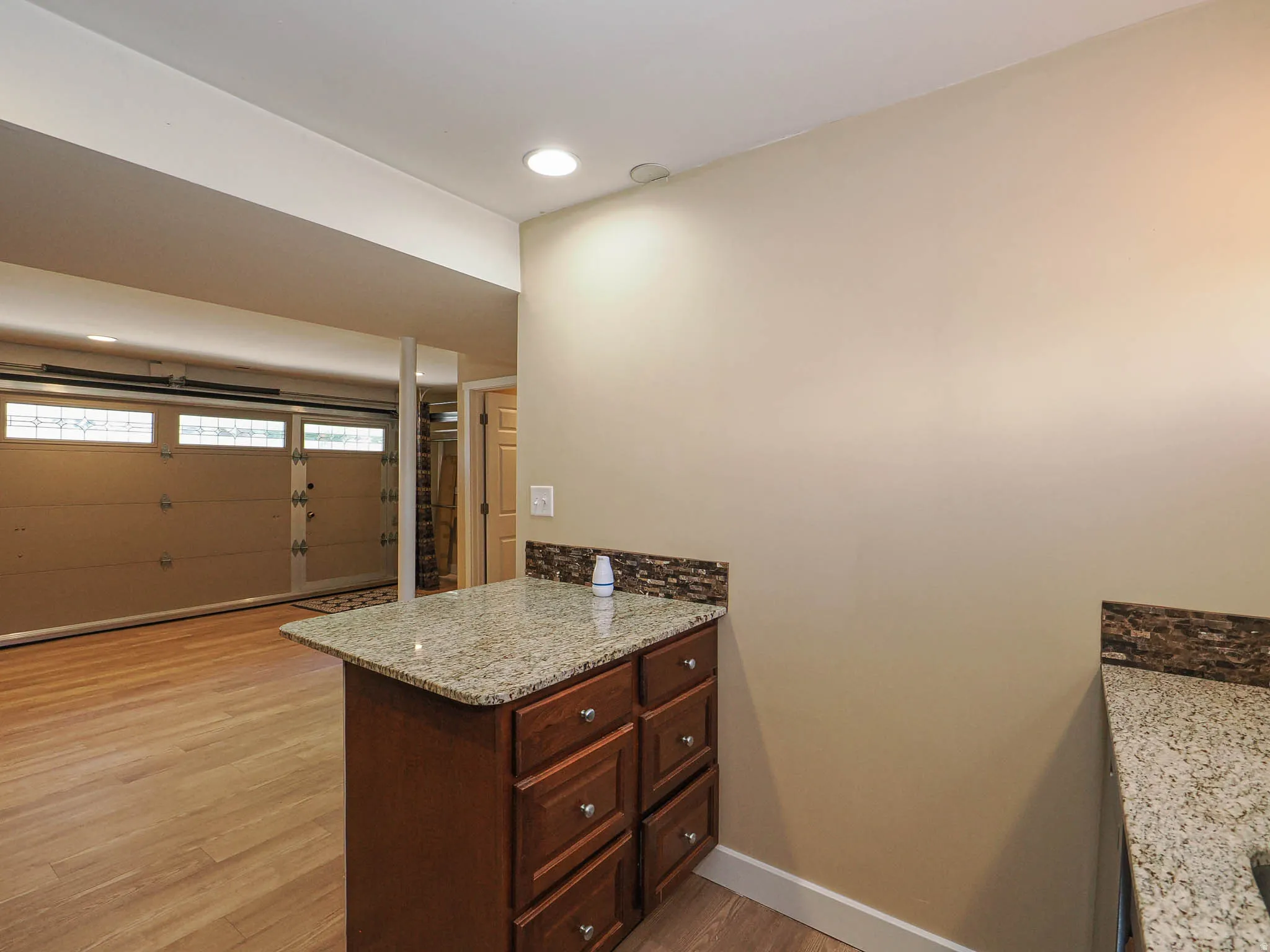 Functional space featuring wood-finish flooring, recessed lighting, and a built-in cabinet with a granite countertop and stone-tiled backsplash