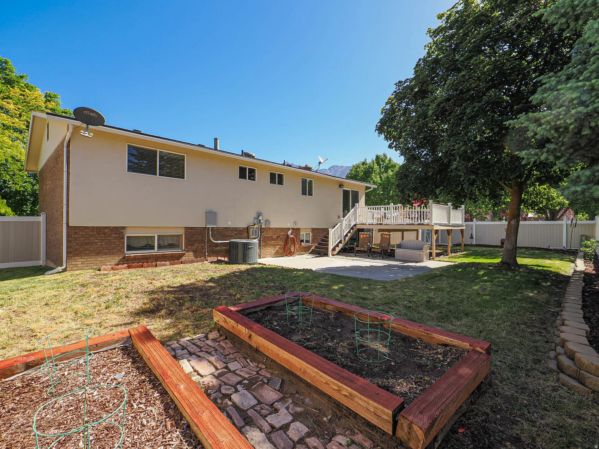 Expansive backyard featuring a multi-level deck, a concrete patio, a mature tree, and raised garden beds with stone pathway