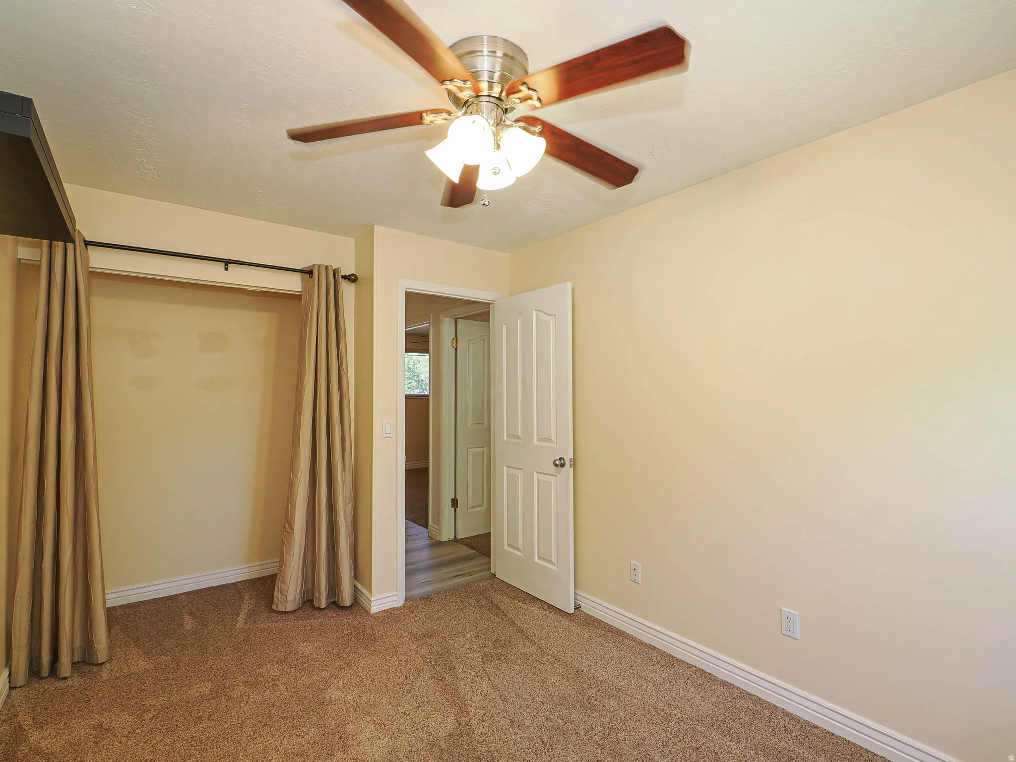 Carpeted interior space featuring a ceiling fan with integrated lighting, a solid white interior door, and a curtained alcove