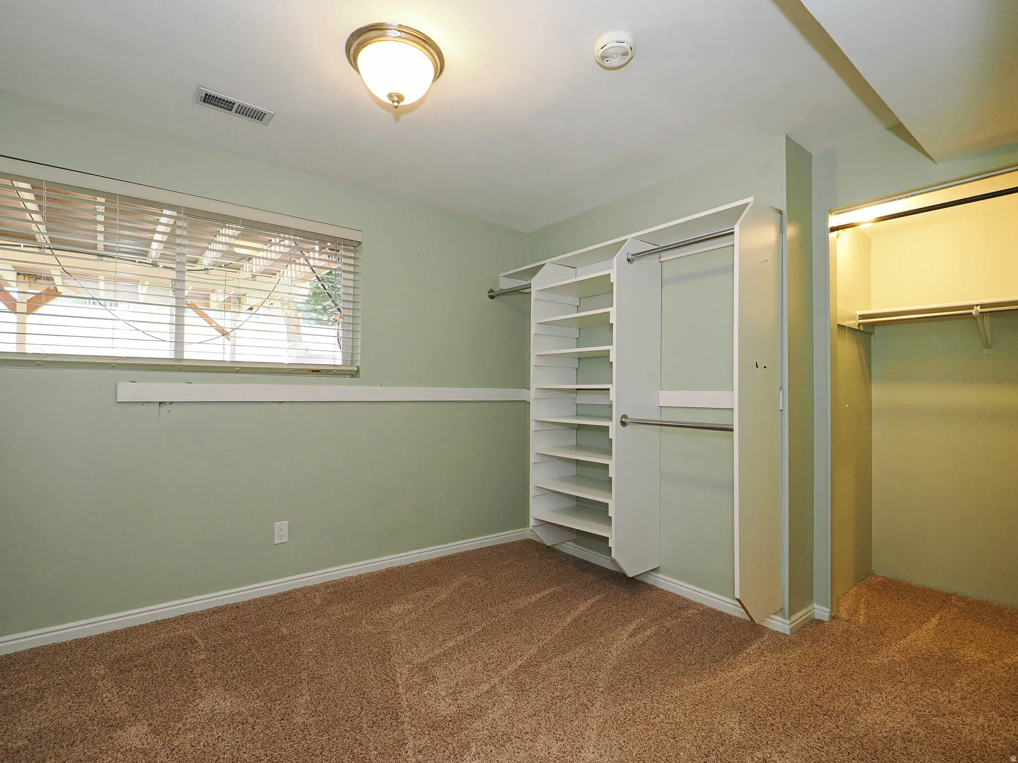Room featuring light green walls, brown carpet flooring, and a window with horizontal blinds