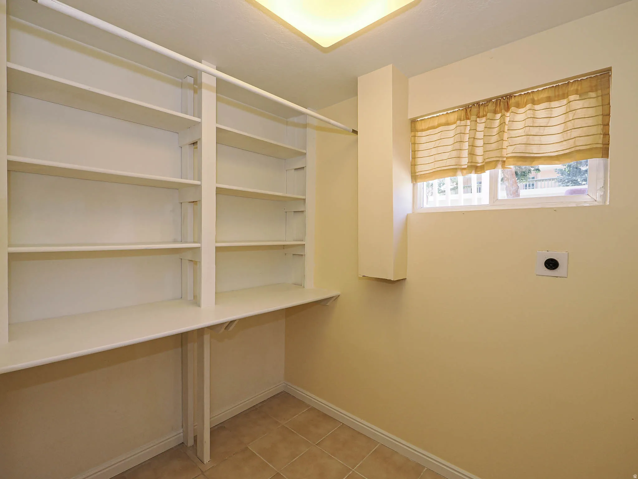 Utility area featuring built-in shelving, a wall-mounted hanging rod, tile flooring, and a rectangular window