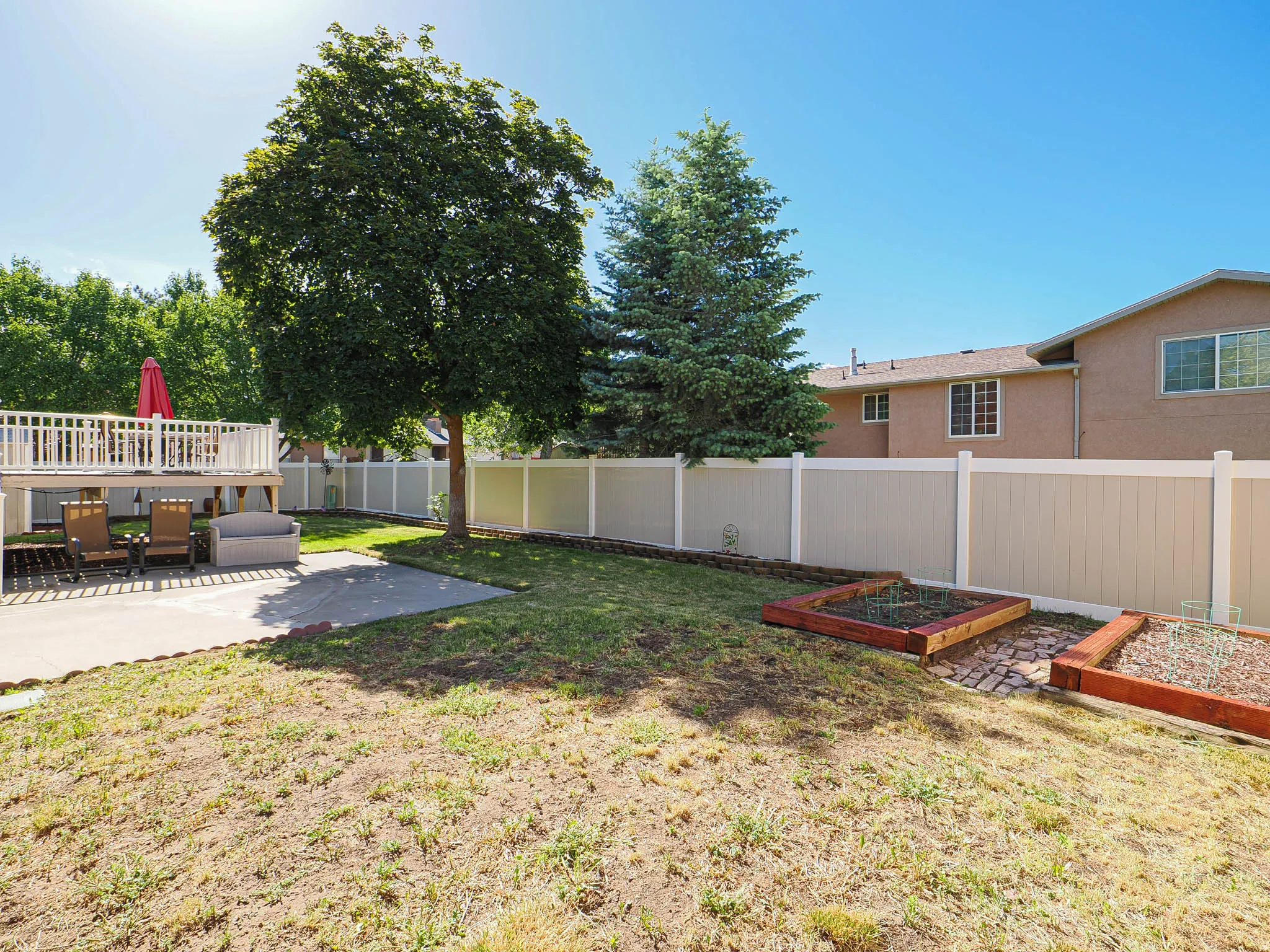 Spacious backyard featuring a two-tier deck, concrete patio, mature trees, privacy fencing, and built-in garden beds