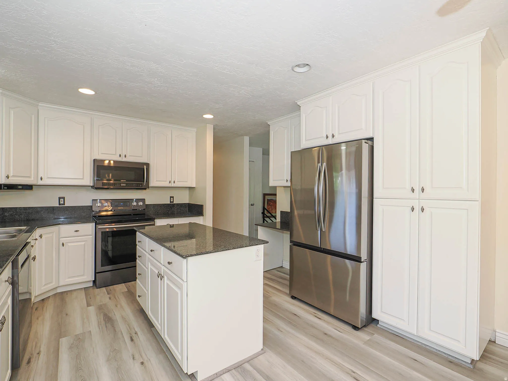 Kitchen featuring white cabinetry, dark stone countertops, stainless steel appliances, a central island, and wood-finish flooring