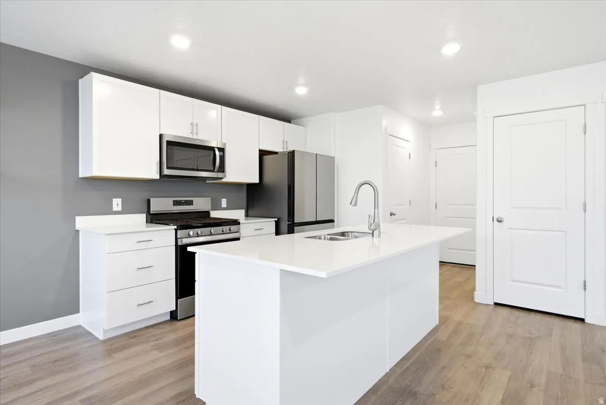 Modern kitchen featuring white cabinetry, a large kitchen island with an integrated sink, stainless steel appliances, and wood-finish flooring
