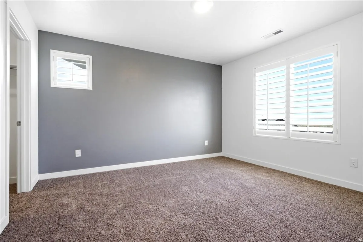 Carpeted room featuring a single accent wall, white baseboards, and two windows