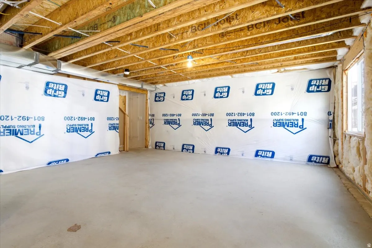 Unfinished basement featuring exposed wood joists, a poured concrete floor, and insulated walls