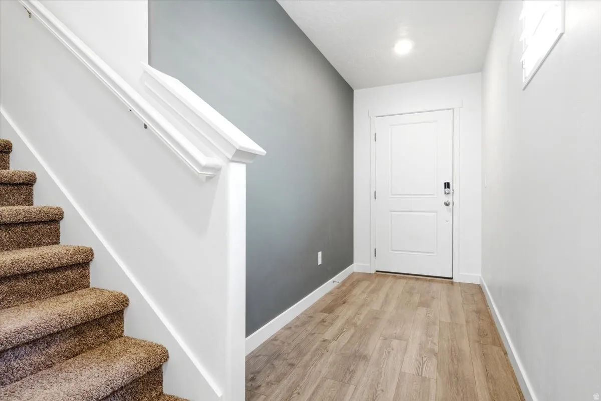Entryway featuring wood-finish flooring, a white paneled door with hardware, and overhead lighting