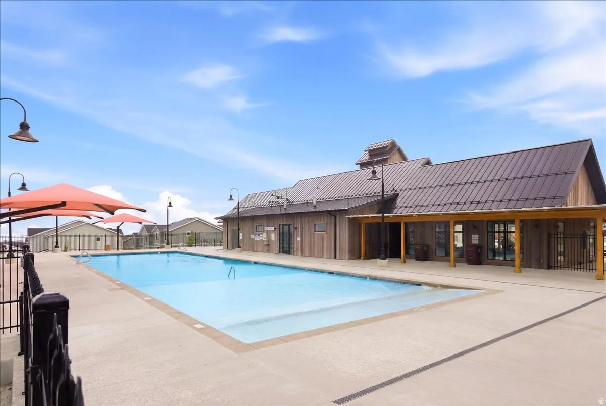 Expansive outdoor swimming pool with surrounding concrete decking, shaded by large orange canopies, and bordered by a black metal fence