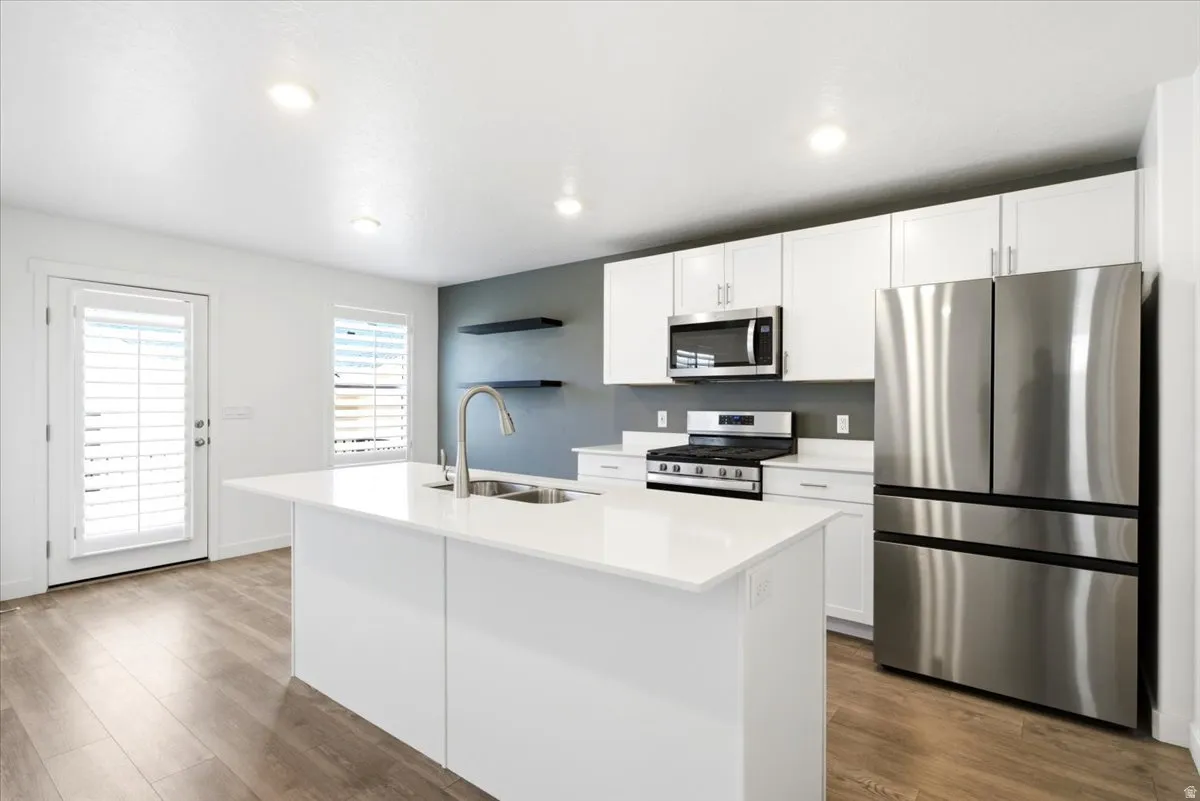 Contemporary kitchen featuring a large central island with an integrated sink, white cabinetry, stainless steel appliances, and wood-finish flooring