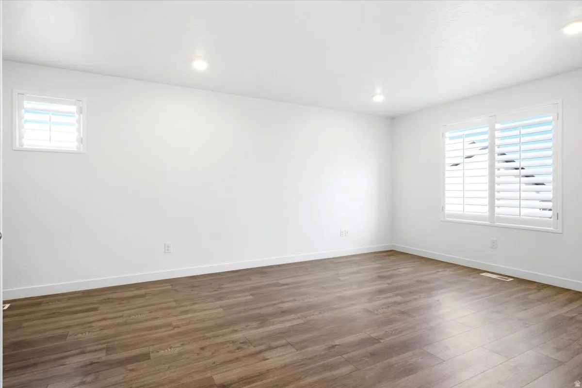 Spacious room featuring wood-finish flooring, white baseboards, and bright white walls