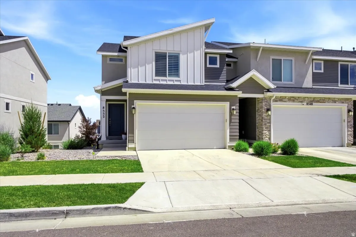 Modern two-story home featuring a clean contemporary exterior with mixed siding materials in neutral tones, peaked rooflines with architectural interest, and a spacious two-car garage with white panel doors