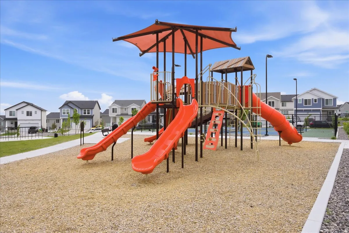 Community playground featuring multiple slides, climbing structures, a protective canopy, and a wood chip surface
